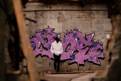 人在白色套衫连帽衫靠在紫色的涂鸦墙
